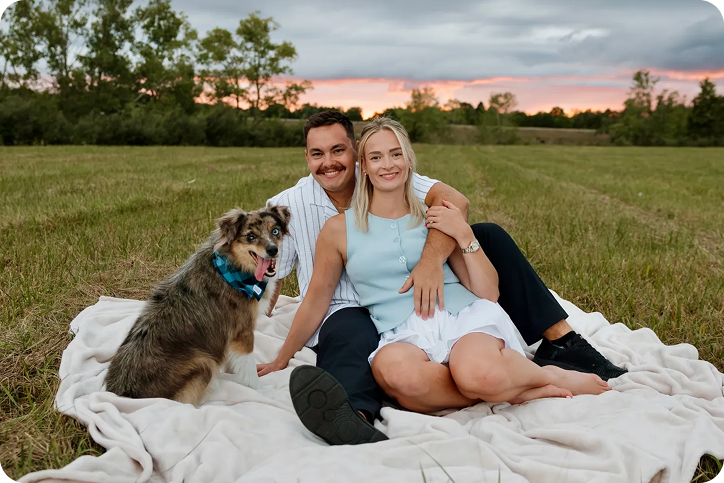 Smiling couple with dog on blanket at sunset
